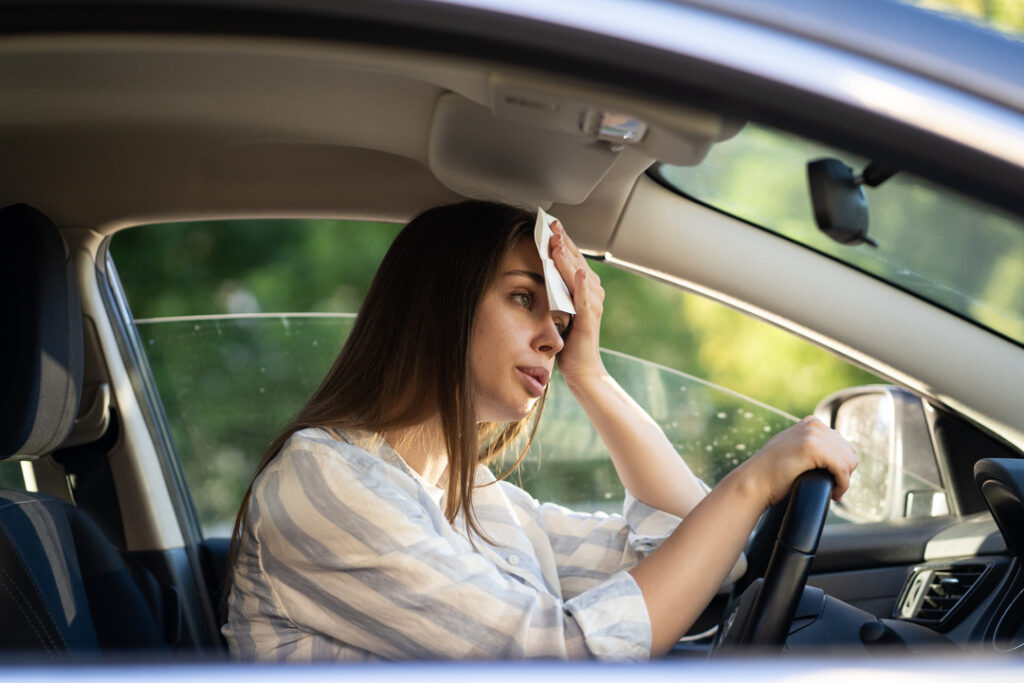 Girl driver being hot during heat wave in car, suffering from hot weather, has problem with a non-working air conditioner, wipes sweat from her face with tissue. Summer, heat concept.