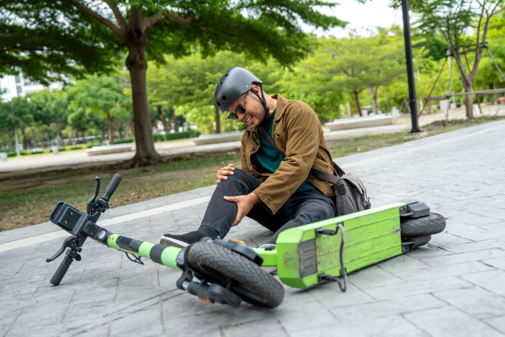 Young Asian Businessman falling off EV scooter on the road. Accident Injury leg pain. Broken leg falls off the Scooter. Accident on the road.