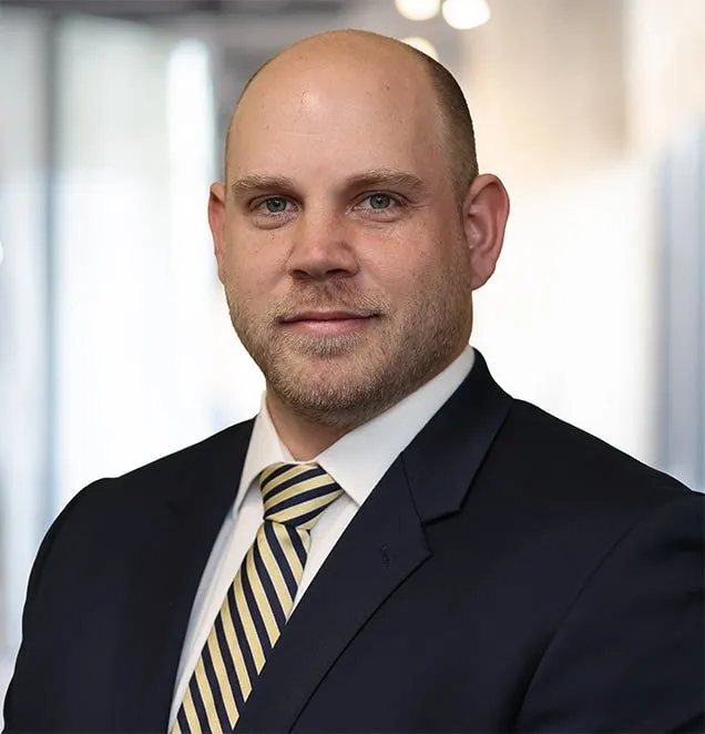 Professional headshot of a man in navy suit and striped tie in modern office setting.