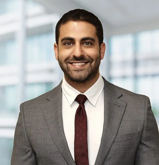 Professional headshot of a man in gray suit and burgundy tie smiling in modern office setting.