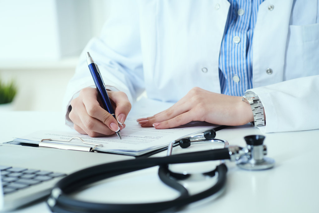 Mid section of female doctor writing prescription to patient at worktable.