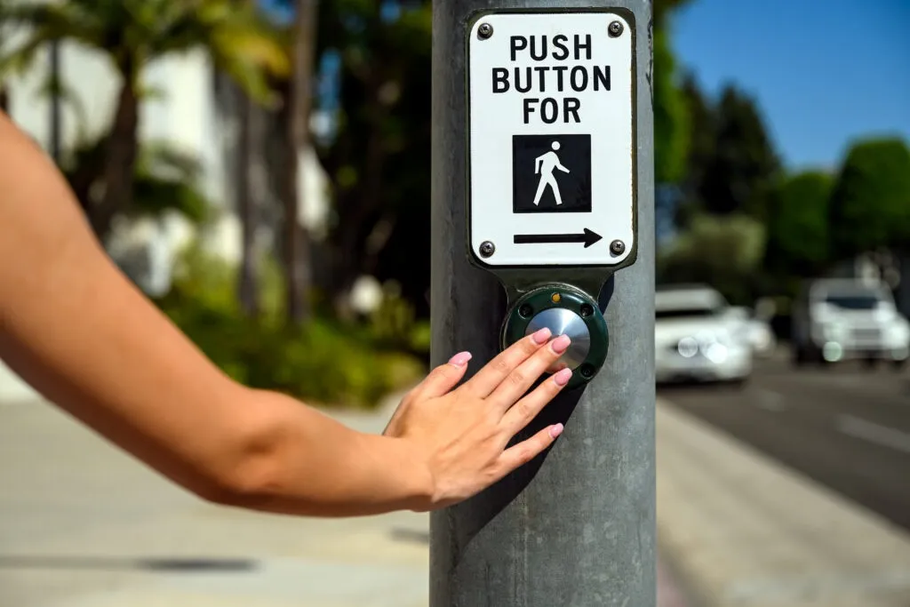 Push button to cross with sign, hand. Pedestrian crossing crosswalk. Female pushing a button to stop car traffic in an intersection.