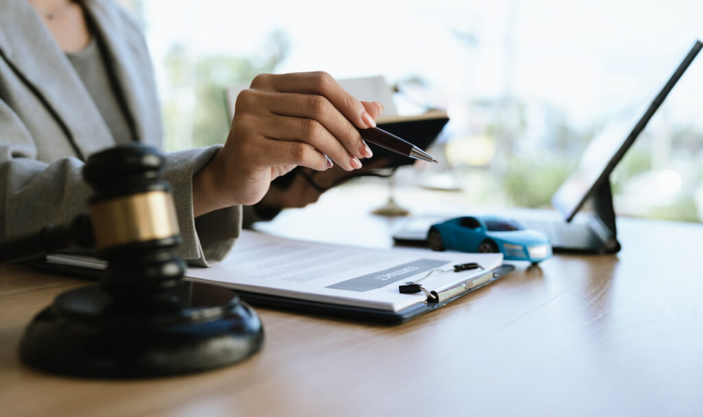 A lawyer signing a car contract with a gavel and a toy car on the desk, symbolizing car law, insurance, or legal agreement.